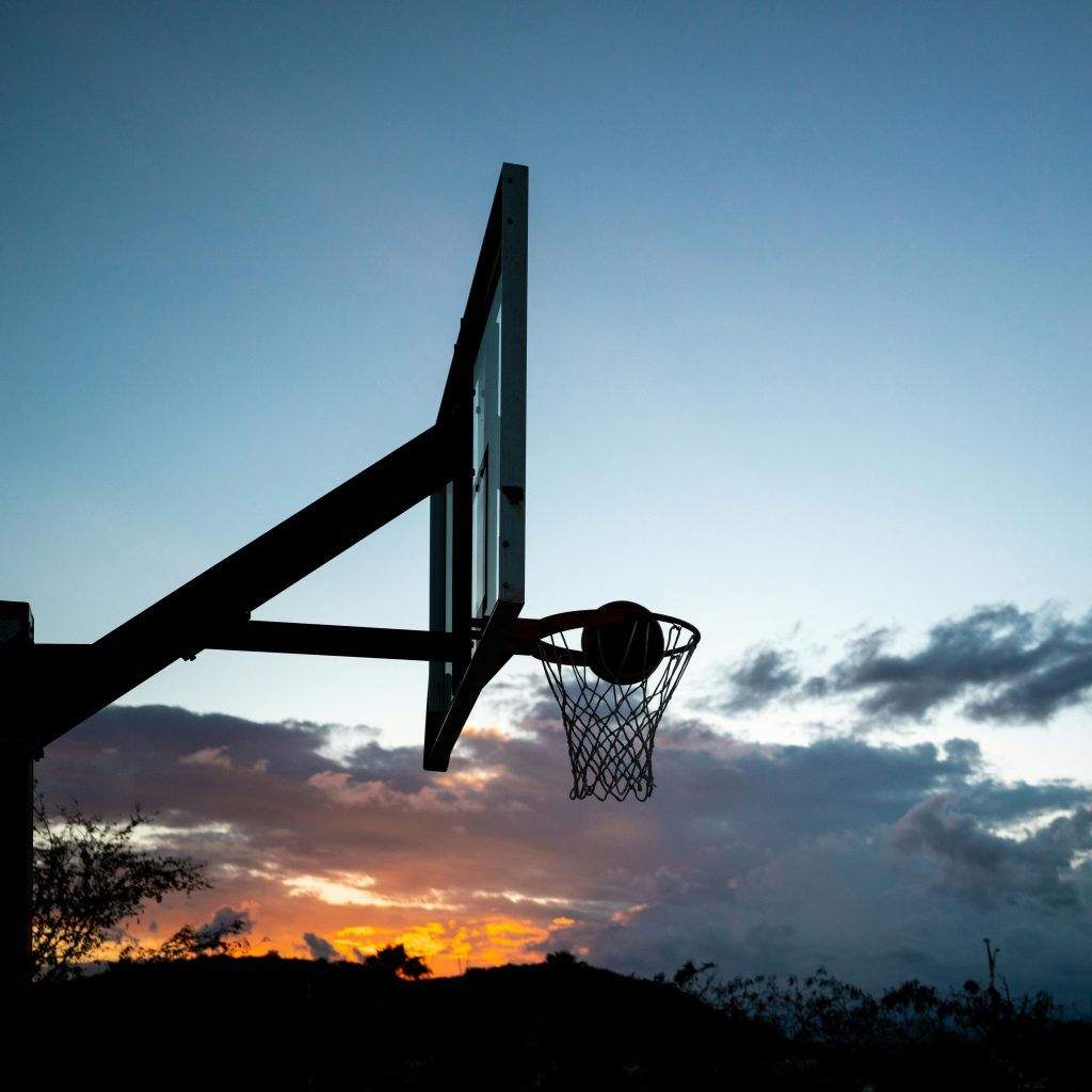 A basketball hoop silhouette with a ball against a stunning sunset sky, capturing the essence of outdoor sports.